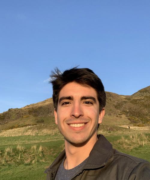 新男友Storni的照片, 微笑, 穿着灰色t恤和棕色夹克, 以蓝天和草山为背景