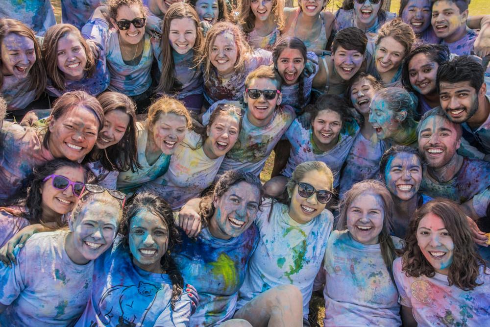 A large group of students affiliated with South Asian Student Association smiles at the camera while covered in dye following their annual Holi celebration
